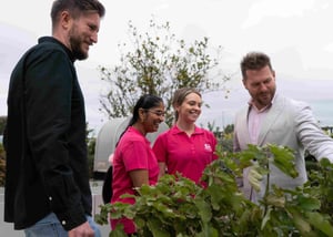Josh, Ed and two nurses discussing by a flower bed or vegetable garden smiling and pointing