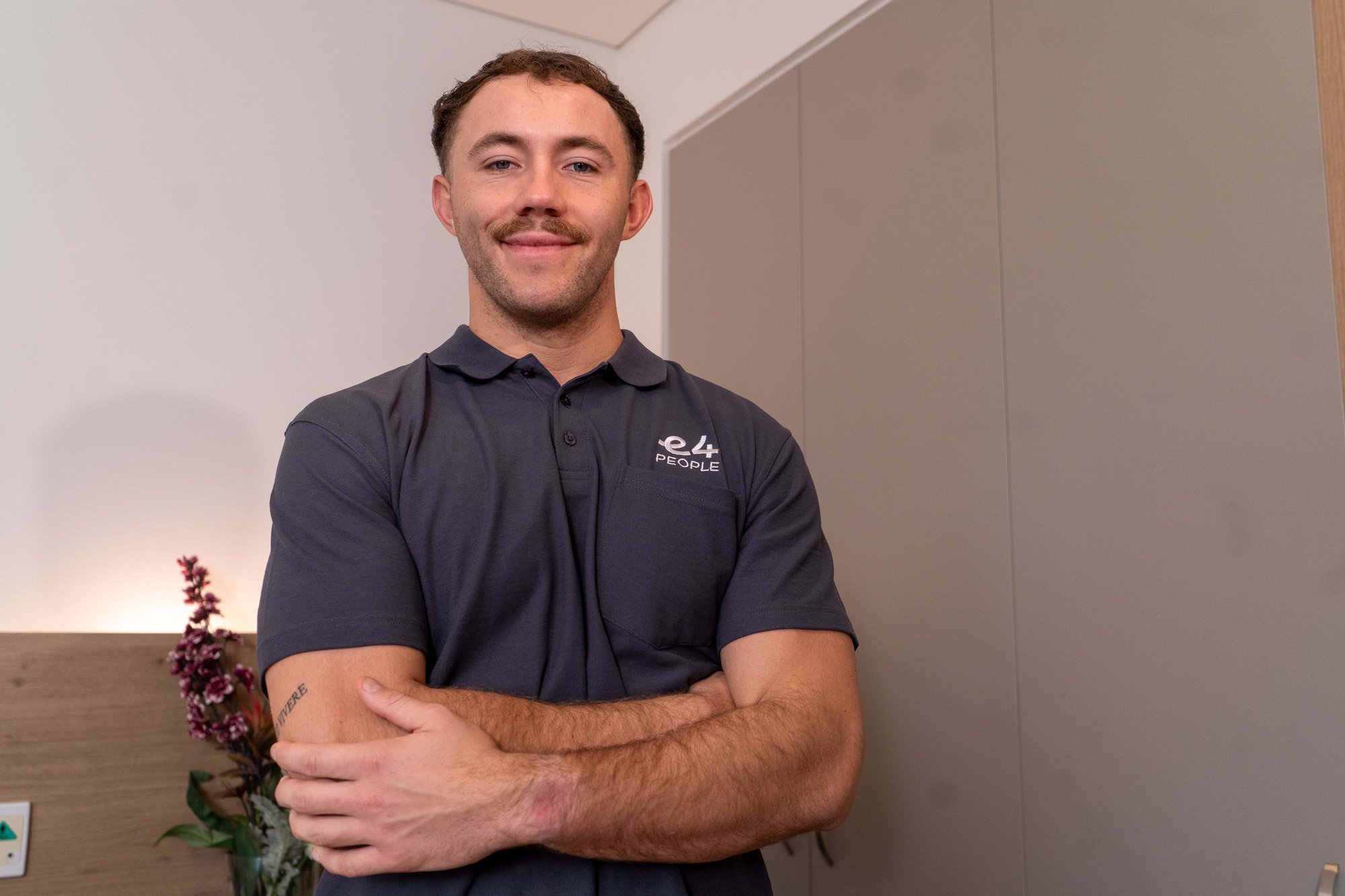 Male E4 nurse in grey uniform smiling looking to camera arms folded