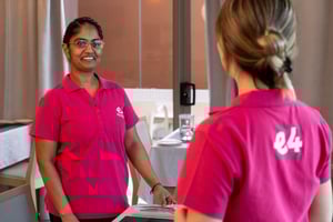 Two E4 nurses, back shot of one with E4 logo on back on pink uniform, talking to eachother in dining room 3